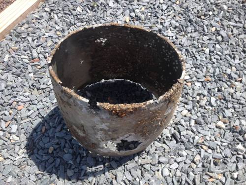 A rusty, damaged metal container sitting on a bed of small gray stones.