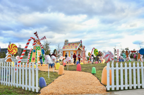 A whimsical candy-themed scene with a gingerbread house, oversized sweets, and visitors enjoying the festive atmosphere.
