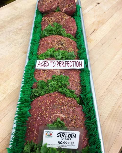 A tray of sirloin steaks garnished with kale, labeled "Aged to Perfection" and priced at $10.99 per pound.