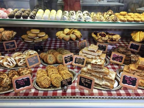 A display case filled with various baked goods, including cookies, pastries, and cakes, on a checkered tablecloth.