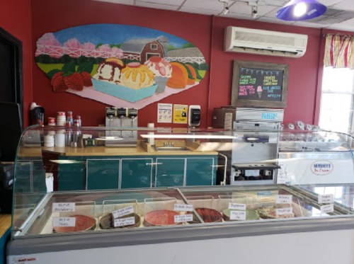 A colorful ice cream shop interior featuring a display of various ice cream flavors and a mural of a barn and strawberries.