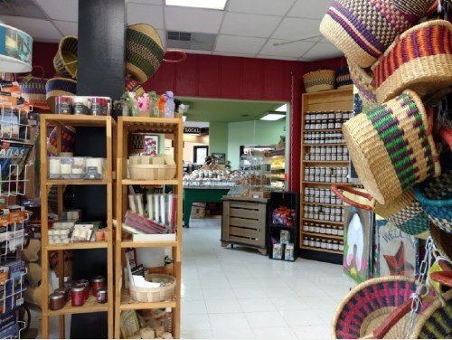 A colorful store interior featuring shelves of candles, woven baskets, and jars, with a view into a food area.