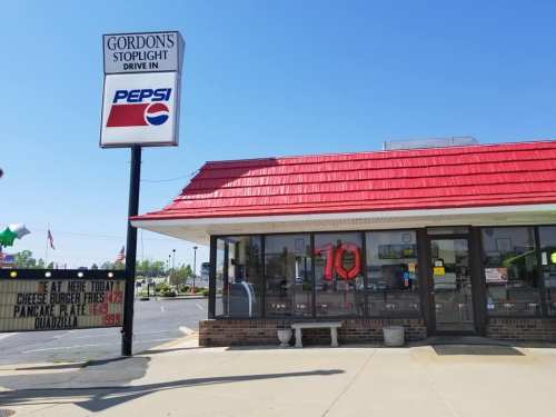 Exterior of Gordon's Stoplight Drive-In with a red roof, sign displaying menu items and prices, and a clear blue sky.