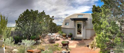 A cozy dome-shaped home surrounded by greenery and potted plants, with a small outdoor seating area.