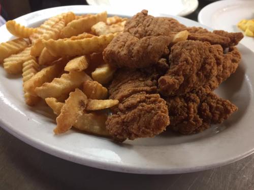 A plate of crispy fried chicken strips served with crinkle-cut fries.