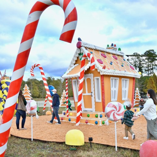 A whimsical gingerbread house surrounded by oversized candy decorations and visitors enjoying the festive scene.