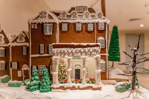 A detailed gingerbread house with white icing, colorful decorations, and green trees, set on a snowy surface.