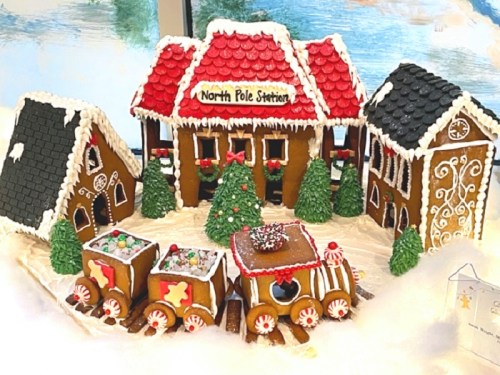 A festive gingerbread village featuring a North Pole station, decorated houses, trees, and a train made of gingerbread.