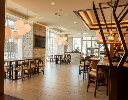 Modern restaurant interior with wooden tables, chairs, and unique pendant lighting, featuring large windows and a warm atmosphere.