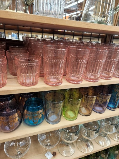 A display of colorful glassware, including pink and patterned glasses, arranged on wooden shelves.
