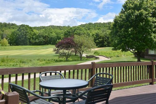 A scenic view from a deck overlooking a green golf course and trees under a partly cloudy sky.