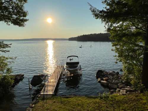 A serene lake view at sunset, featuring a dock with a boat and paddleboarders in the distance.