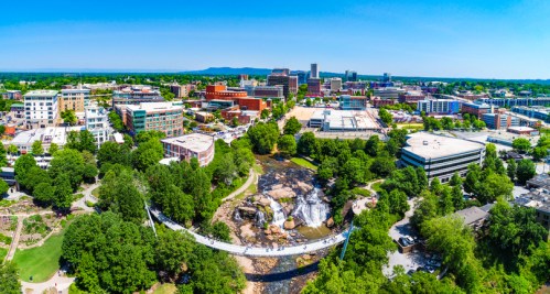 Aerial view of a city with a waterfall, greenery, and buildings under a clear blue sky.