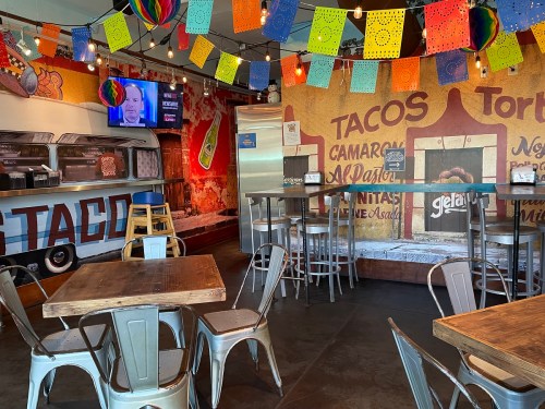 Colorful taco restaurant interior with festive decorations, tables, and a TV displaying a program.