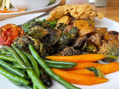 A plate of crispy fried chicken, roasted potatoes, Brussels sprouts, green beans, and carrots.