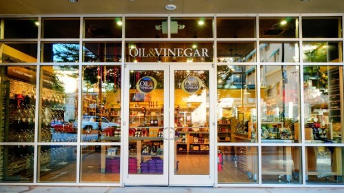 Storefront of an oil and vinegar shop with large glass windows displaying various products inside.