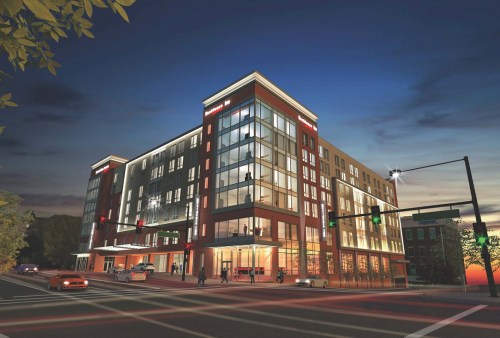 A modern multi-story building with large windows, illuminated at dusk, located at a street intersection.