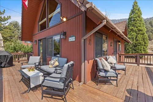 Cozy wooden deck with seating, overlooking a scenic view, featuring a brown chalet-style house and greenery.