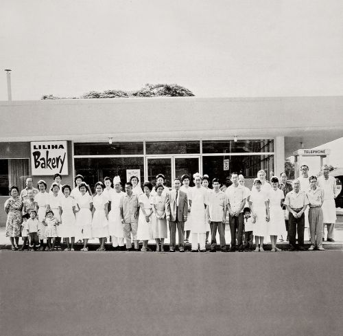 A large group of people poses outside Liliha Bakery, showcasing a mix of ages and styles in a historic black-and-white photo.