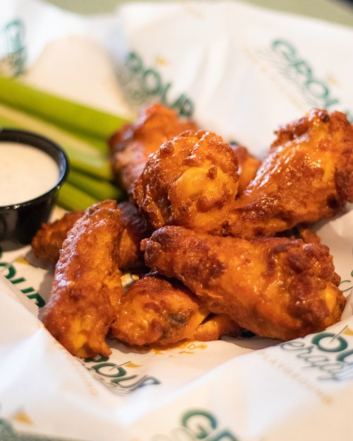A basket of crispy chicken wings with celery sticks and a side of dipping sauce.