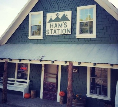 A rustic green building with a sign reading "Ham's Station," featuring pumpkins and an "Open" sign.