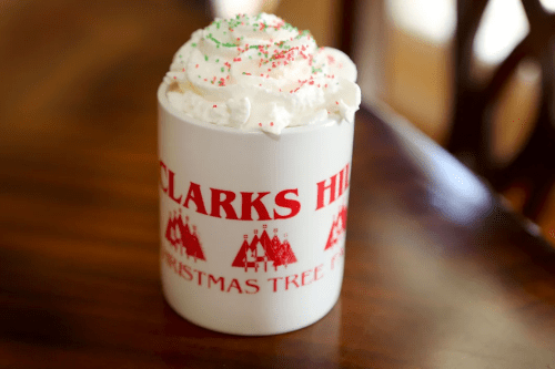 A festive mug filled with whipped cream and sprinkles, sitting on a wooden table.