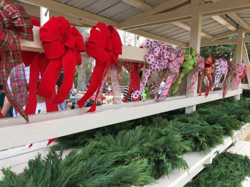 Colorful bows in various patterns hang on a shelf above fresh greenery, creating a festive display.