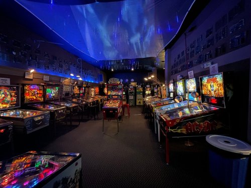 A vibrant arcade filled with pinball machines, colorful lights, and a starry ceiling, creating a lively atmosphere.
