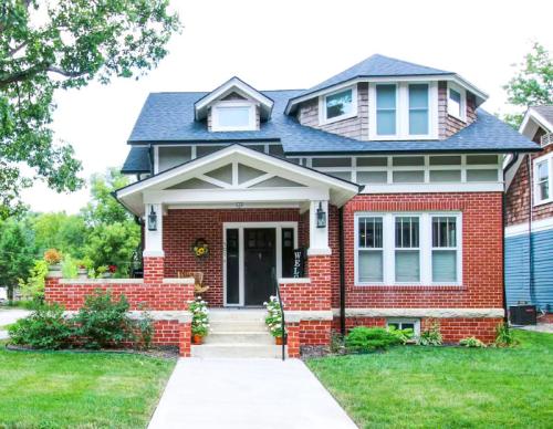 A charming two-story brick house with a front porch, surrounded by greenery and a well-maintained lawn.