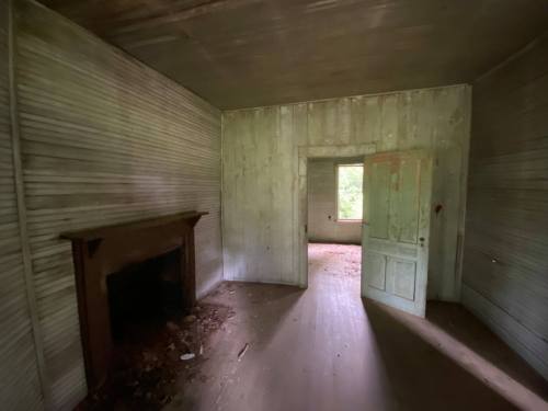 An empty, weathered room with peeling walls, a fireplace, and an open door leading to another room.