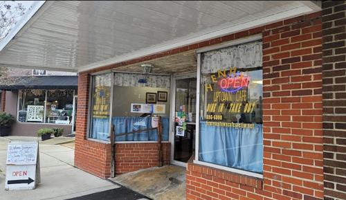 A brick storefront with large windows displaying "OPEN" signs and a blue curtain, inviting customers inside.