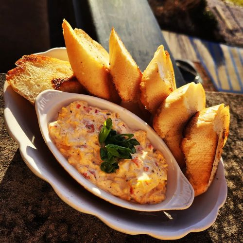 A dish of creamy dip topped with herbs, served with toasted bread slices on the side.