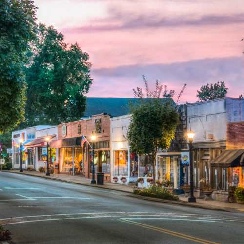 A charming street lined with shops and trees, under a colorful sky at dusk.