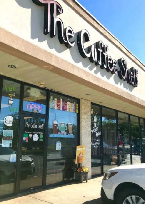 Exterior of "The Coffee Shelf" with large windows displaying menu items and an "OPEN" sign. Sunny day.