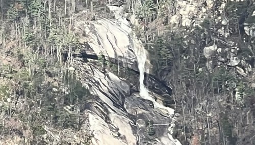A waterfall cascading down a rocky cliff, surrounded by sparse trees and rugged terrain.