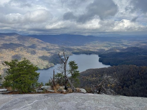 A panoramic view of a lake surrounded by mountains and trees under a cloudy sky.