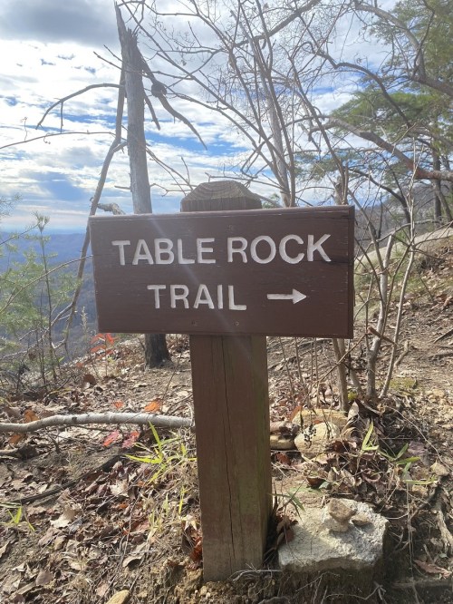 Wooden sign pointing to "Table Rock Trail" with a scenic view in the background and sparse trees around.