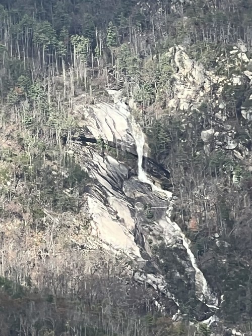 A waterfall cascading down a rocky mountain slope, surrounded by sparse trees and rugged terrain.