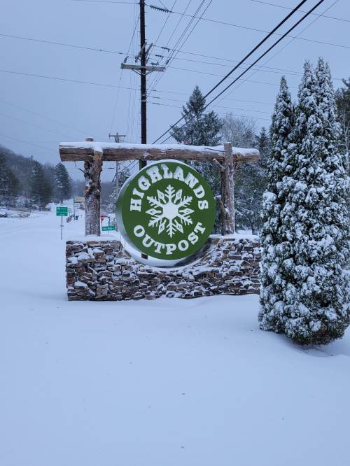 A snowy scene featuring a sign for "Highlands Outpost" surrounded by snow-covered trees and a winter landscape.