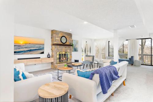 Bright, modern living room with a stone fireplace, large windows, and cozy furniture, featuring a beach scene on the TV.