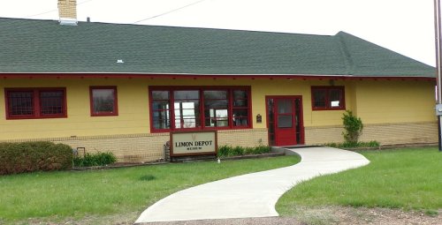 A yellow building with red trim, labeled "Limon Depot Museum," surrounded by green grass and a concrete walkway.