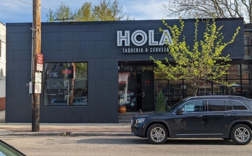 Exterior of Hola Taqueria & Cerveza, featuring a modern black facade and a parked car in front.