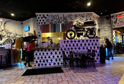 A vibrant restaurant interior with artistic murals, a bar area, and a bicycle display above the counter.