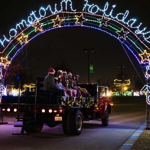 A festive scene with a decorated truck and people in Santa hats under a glowing "Hometown Holidays" arch.