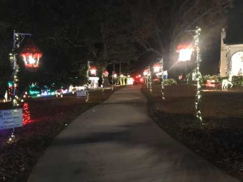 A festive pathway lined with illuminated lanterns and holiday decorations, leading through a decorated yard at night.