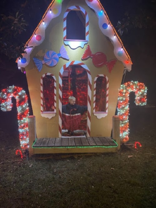 A brightly lit gingerbread house decorated with candy canes and colorful lights, set in a dark outdoor environment.
