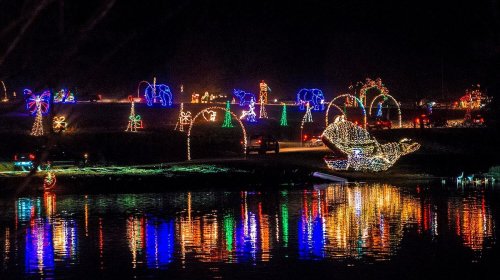 Colorful holiday lights illuminate a festive scene by the water, reflecting on the surface at night.