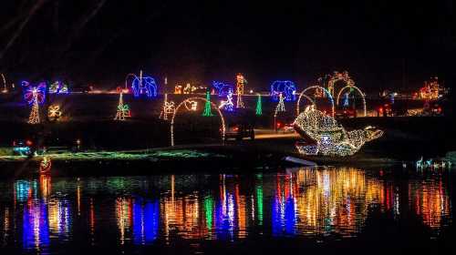 Colorful holiday lights illuminate a festive scene by the water, reflecting on the surface at night.