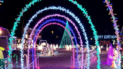 Colorful holiday lights create an archway leading to a festive display with a Christmas tree and decorations.