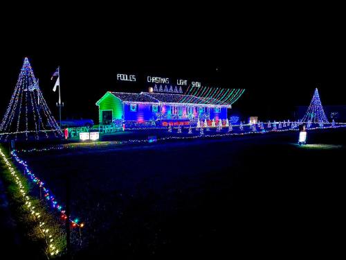 A brightly lit house decorated with colorful Christmas lights, featuring trees and festive displays in a nighttime setting.